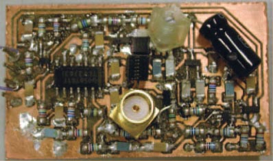 A prototype version of a super-regenerative receiver uses mostly surface-mount components. The large, black, leaded component in the upper right corner is a power-supply-decoupling capacitor. Note the RF-input connector in the center of the pc board.