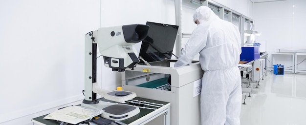 Бесплатное фото Заводской рабочий в белых лабораторных костюмах и масках для лица работает с современным оборудованием в чистой белой комнате, на переднем плане находится электронный микроскоп.